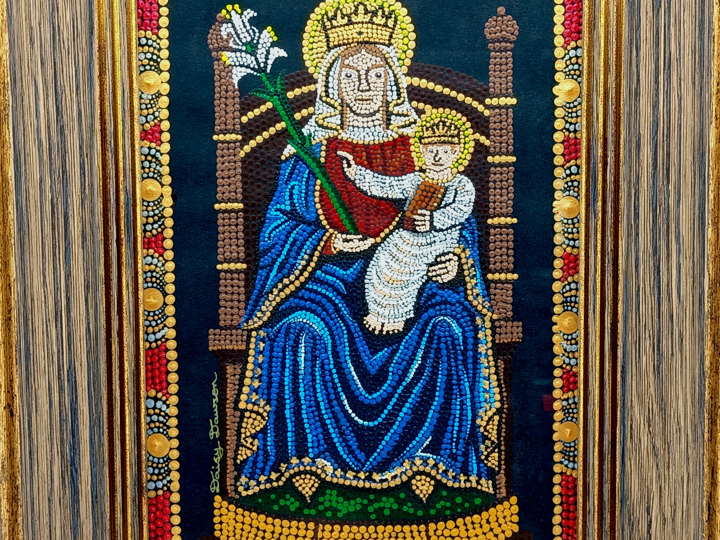 A framed religious mosaic artwork depicting the Madonna and Child on a dark background, with the mother in a blue robe and child in white, surrounded by ornate gold, red, and silver decorative borders.