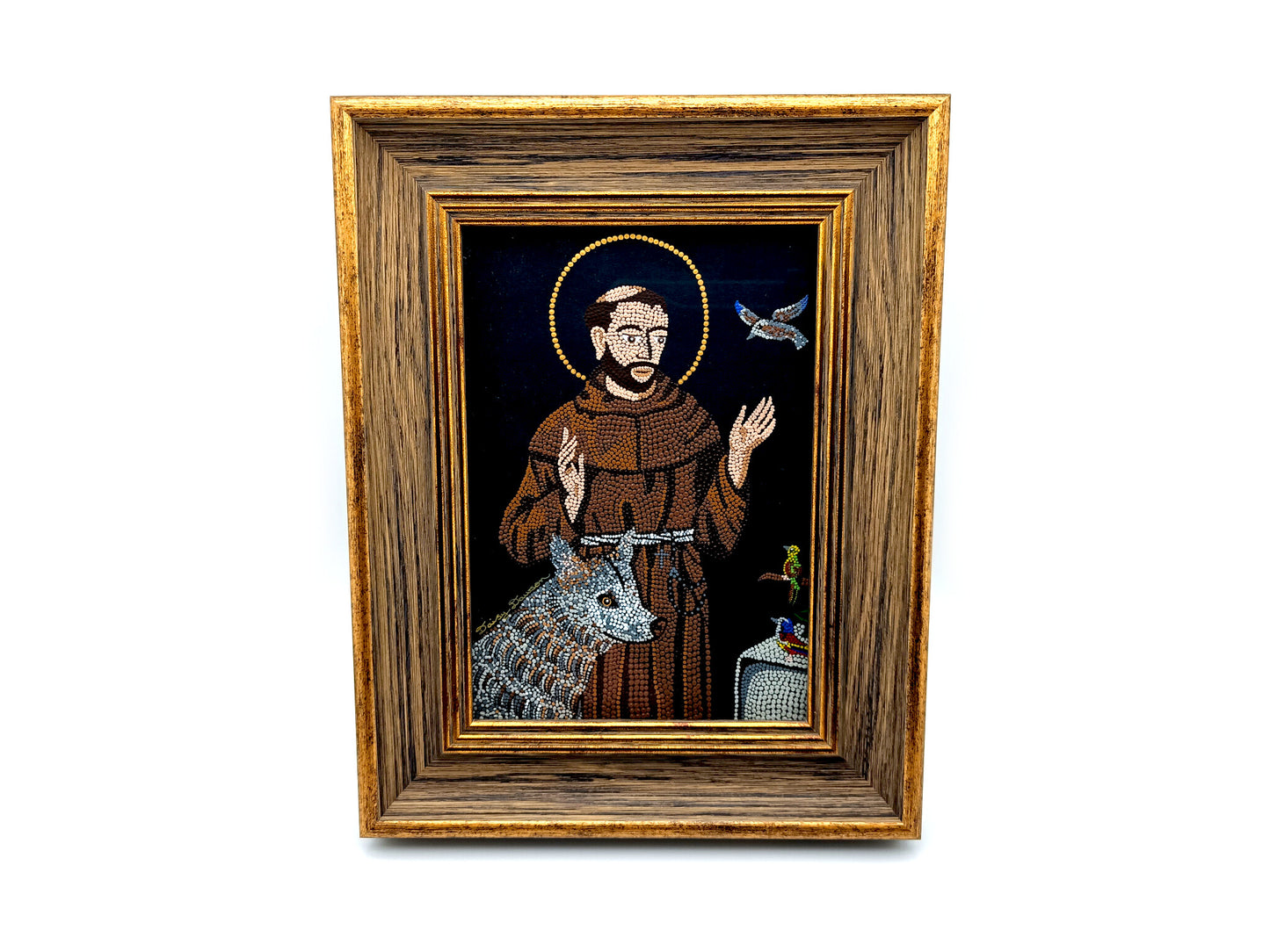 A framed religious icon depicting Saint Francis of Assisi with a brown robe, gold halo, and a silver wolf on a dark background, enclosed in a rustic brown wooden frame with gold trim.