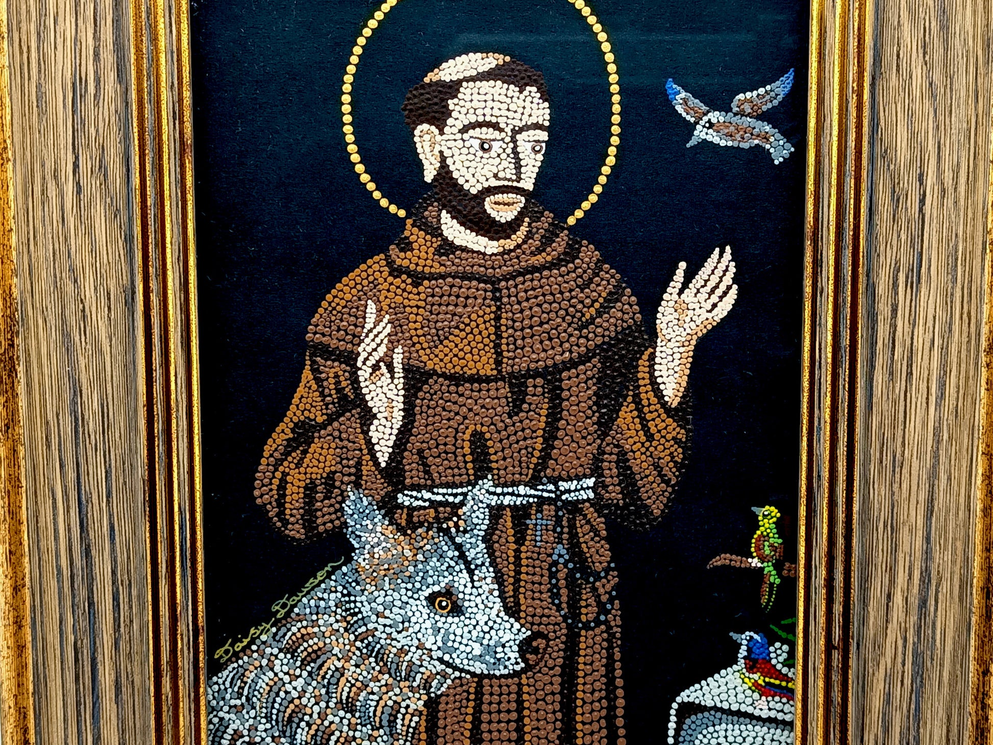 A framed mosaic religious artwork depicting Saint Francis of Assisi in a brown robe with a gold halo, alongside a wolf, dove, and small birds, set within a wood-grain frame.